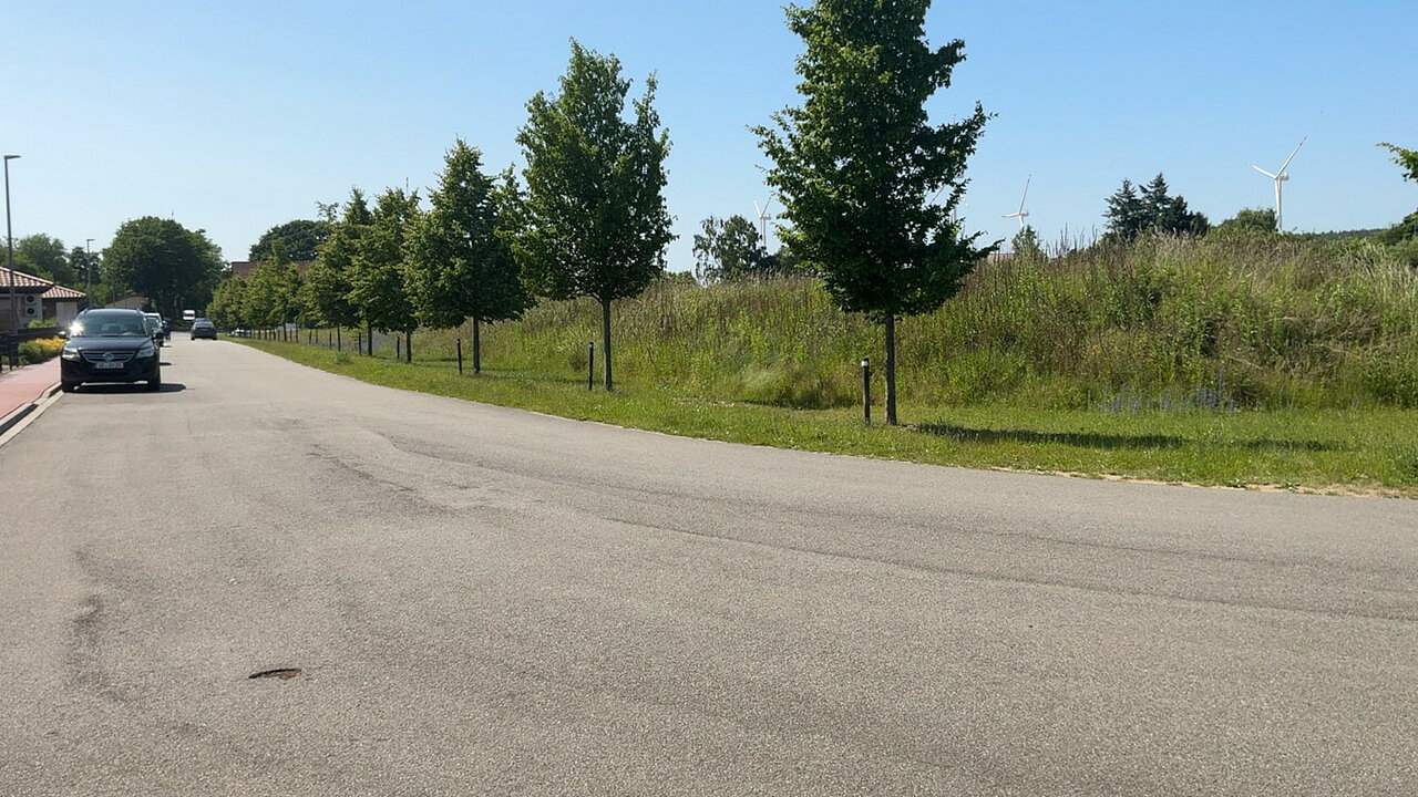 Straße am Rande eines Wohngebietes mit Windenergieanlagen im Hintergrund