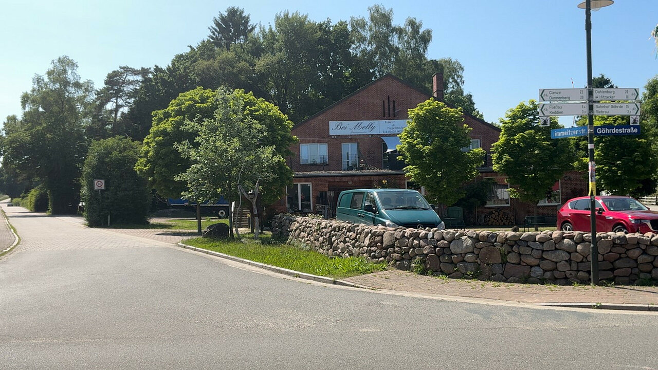 Straßenkreuzung mit einer Gewerbeimmobilie und Parkplatz mit parkenden Autos im Vordergrund.