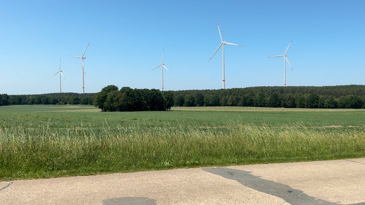 Feldweg am Acker mit Windenergieanlagen hinter dem Wald am Horizont