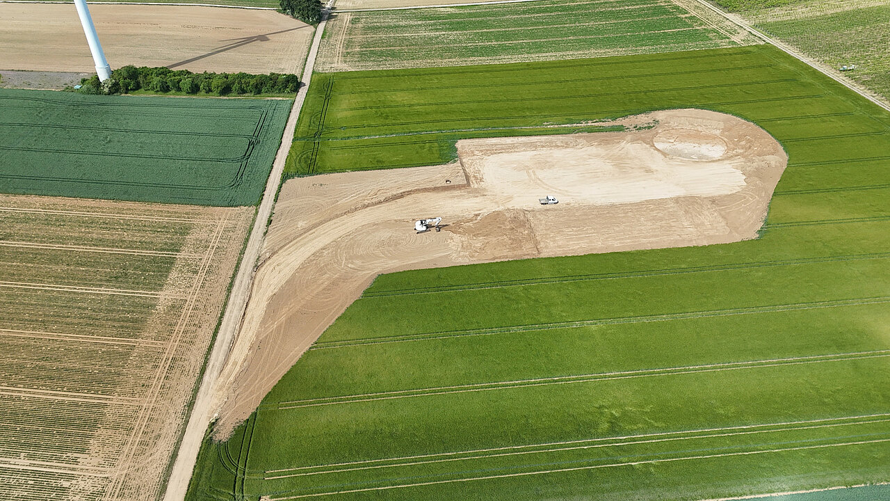 Ein Bagger und ein LKW bereiten die Kranstellfläche vor und heben das Fundament für eine Windenergie-Anlage aus.