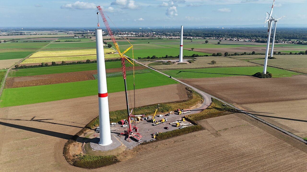 Sind die Fundamente ausgehärtet folgt der Beton-Turmbau der beiden Windenergie-Anlagen. Im Vordergrund wird an einer Windenergie-Anlage gebaut. Ein Kran bringt die einzelnen Betonturmteile an.