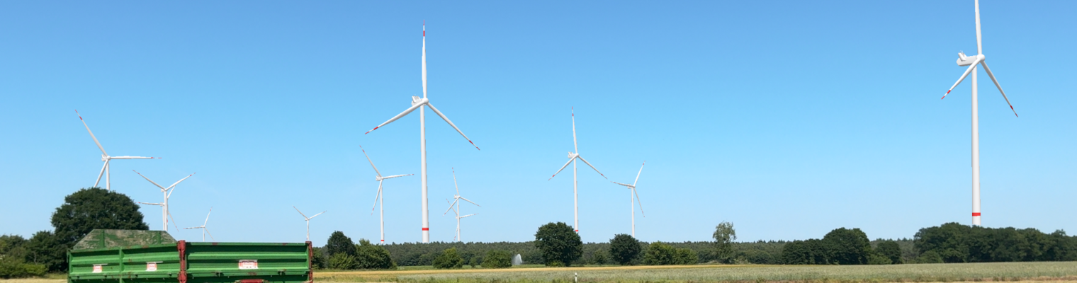 Grüner geparkter Traktoranhänger im Vordergrund. Am Horizont sind Windräder zu sehen