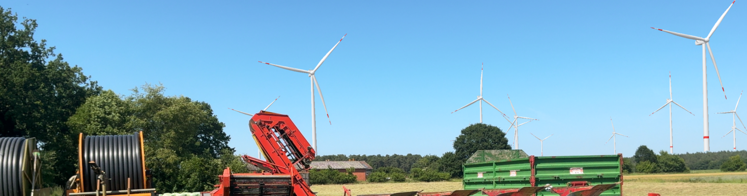 Landmaschinen stehen am Feldrand. Am Horizont sind Windräder zu sehen. 